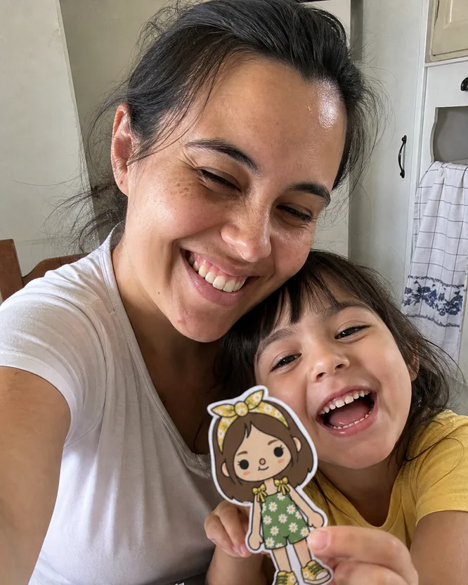 Selfie da Camila com a filha Sophia sentadas na mesa com bonecas de papel